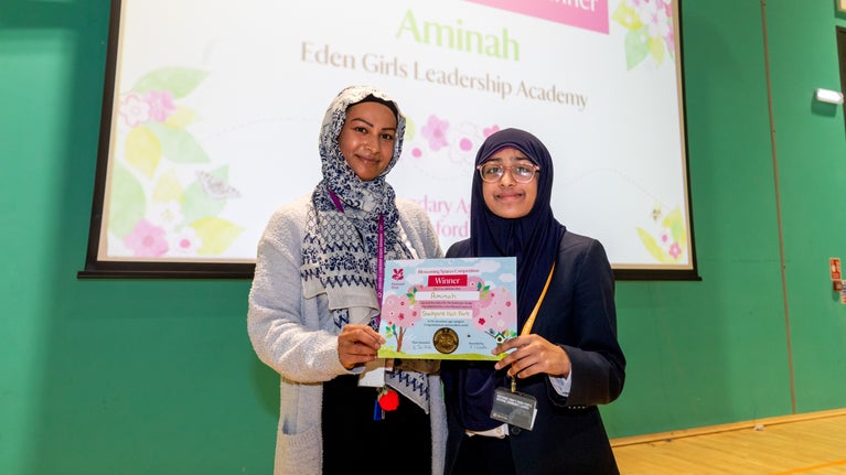 A woman and a child both in headscarves holding a certificate between them. behind them a screen says Aminah Eden Girls leadership Academy
